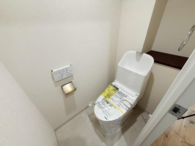 明るい内装で清潔感が漂うトイレです。壁付けの操作パネルで使いやすさに配慮されています。手洗い付きのデザインで機能面にもこだわりを感じられます。収納棚が設けられ空間を有効活用できます。