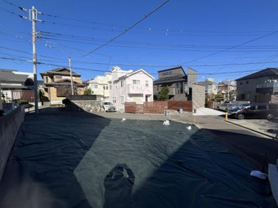 住宅街の一角に位置する現地土地写真です。周辺は整然とした街並みが広がり前面道路も広々としています。日当たりが良好で開放感のある空間が魅力です。閑静な住宅街にあり落ち着いた雰囲気が感じられます。