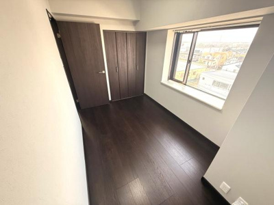 大きな窓から日差しが入る洋室です。ダークブラウンの床が落ち着いた雰囲気を演出します。収納スペースも備わっており空間を有効活用できます。シンプルな内装でインテリアのアレンジがしやすいお部屋です。