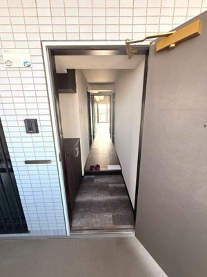 玄関からまっすぐ伸びる廊下が室内の奥行きを感じさせます。シンプルなタイル外壁とドアの組み合わせが印象的です。シューズ収納スペースも備わっておりすっきりとした印象を与えます。