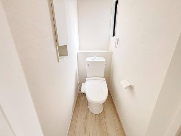 シンプルで清潔感のあるトイレ空間です。窓が設けられているため自然光が差し込み明るい印象となっています。壁付けの収納スペースも備わっています。床材がナチュラルな色合いで落ち着いた雰囲気です。
