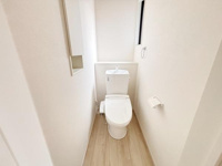 シンプルで清潔感のあるトイレ空間です。窓が設けられているため自然光が差し込み明るい印象となっています。壁付けの収納スペースも備わっています。床材がナチュラルな色合いで落ち着いた雰囲気です。