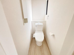 シンプルで清潔感のあるトイレ空間です。窓が設けられているため自然光が差し込み明るい印象となっています。壁付けの収納スペースも備わっています。床材がナチュラルな色合いで落ち着いた雰囲気です。