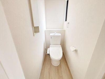 シンプルで清潔感のあるトイレ空間です。窓が設けられているため自然光が差し込み明るい印象となっています。壁付けの収納スペースも備わっています。床材がナチュラルな色合いで落ち着いた雰囲気です。