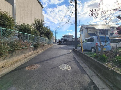 現地前面道路はゆったりとした幅があり車両の出入りもしやすい環境です。舗装された道路が続いており周囲も落ち着いた住宅地です。日当たりの良さが感じられる現地写真です。