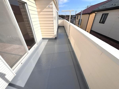バルコニーは広めの設計で日当たりも十分に感じられます。防水仕様の床材が使われておりお手入れも簡単です。外壁と調和した明るいカラーが印象的です。洗濯物を干すスペースもしっかり確保されています。