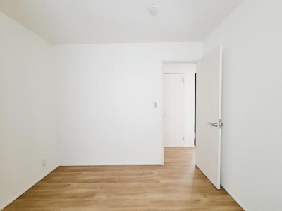 シンプルな内装が特徴の洋室です。白を基調とした壁とナチュラルなフローリングが調和しています。ドアや壁面も明るい色合いで統一されています。落ち着いた雰囲気の空間です。家具のレイアウトもしやすい形状です。