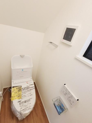 清潔感のある明るいトイレ空間です。換気設備がしっかりと設けられております。床材の木目が温かみを感じさせます。収納スペースも確保されています。窓があり採光も良好です。