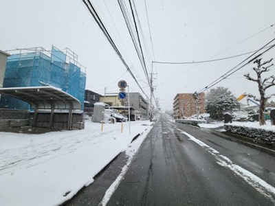 前面道路は見通しが良く歩道も確保されています。周辺には建物が整然と並んでおり整った街並みが広がります。雪景色の中でも道路状況を確認しやすい環境です。周辺にはバス停や駐車スペースも見受けられます。