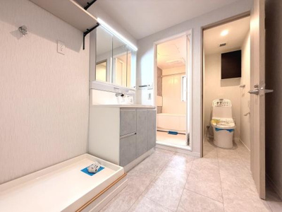 洗面所は明るい照明で清潔感のある空間に仕上がっています。広いカウンターと収納スペース付きで使い勝手が良さそうです。バスルームとトイレへの動線もスムーズな間取りです。