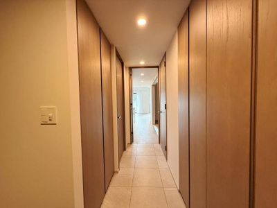 明るい照明が廊下をやさしく照らしています。ナチュラルな木目調の建具が落ち着いた雰囲気を演出します。すっきりとしたデザインで空間全体が広く感じられます。収納スペースも豊富に確保されています。