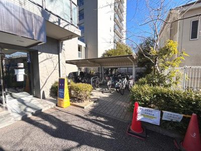 エントランス付近には自転車置き場が設けられており雨よけの屋根も備わっています。出入りのしやすい動線が確保されています。敷地内の植栽も整備されています。明るい印象の共用スペースです。
