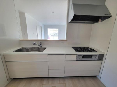 シンプルなデザインが特徴のキッチンです。広々としたワークトップと収納スペースがあります。ガスコンロと換気フードも設置されています。使い勝手を重視したコンパクトな配置です。