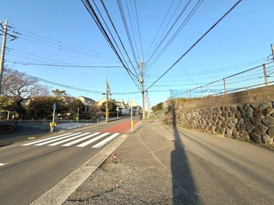 広めの前面道路がしっかりと整備されており歩道も確保されています。明るい日差しが差し込む環境です。周辺には住宅や施設も見え安心感があります。石垣がアクセントとなり景観にも配慮されています。