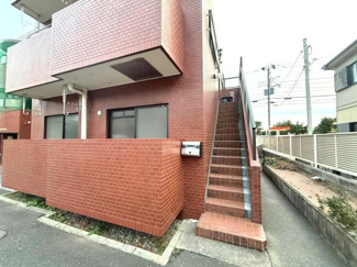 赤茶色のタイル外壁が目を引く建物です。階段部分も同じタイルで統一感があります。便利な位置にポストが設置されています。周囲には歩道が整備されています。建物の外観がおしゃれです。