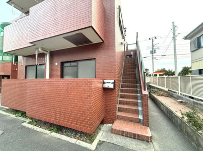 赤茶色のタイル外壁が目を引く建物です。階段部分も同じタイルで統一感があります。便利な位置にポストが設置されています。周囲には歩道が整備されています。建物の外観がおしゃれです。