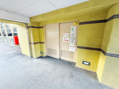 マンションの共用部分で清掃が行き届いた明るい印象のエリアです。壁面のデザインが特徴的で安心感のある雰囲気です。扉周辺には案内や掲示物が丁寧に掲示されています。