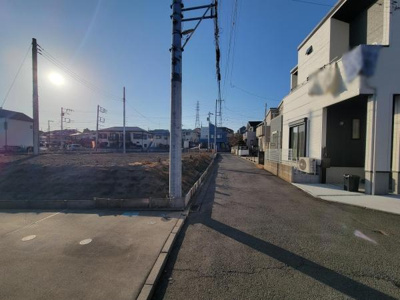 前面道路は舗装されており車の通行もしやすい印象です。周辺は住宅が立ち並び落ち着いた雰囲気です。電柱や配線も整備されています。道路幅があり開放感があります。明るい日差しが差し込む現地写真です。