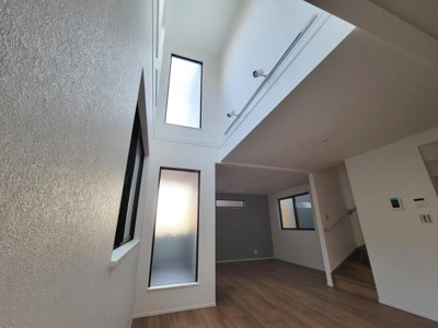 吹き抜けのある空間が広がりを感じさせます。複数の窓からやわらかな自然光が差し込み室内に明るさを与えています。シンプルな内装が開放感を強調します。階段や壁の配置もすっきりとしています。