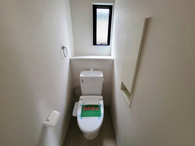 コンパクトなスペースに設置されたトイレです。窓があり換気も可能な設計となっています。シンプルで清潔感のある内装が特徴です。収納スペースもあり使い勝手に配慮されています。