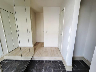 玄関に大きな鏡付き収納が設置されており空間が広く感じられます。白を基調とした明るい内装が魅力です。床の段差とタイル使いが特徴的で清潔感が伝わります。収納扉も複数あり整理がしやすいです。