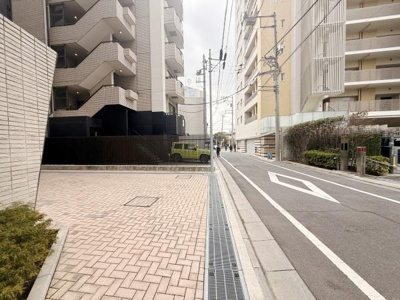 建物外観と前面道路の様子を確認できます。道路幅も十分で周辺環境が整理されています。歩道と車道が分かれているためゆとりを感じられます。周辺には植栽も施されています。