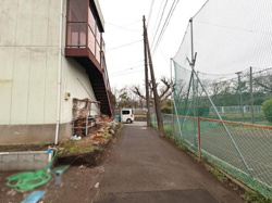 建物の横に広がる舗装された通路があり奥には駐車スペースも確保されています。フェンス越しに隣接するテニスコートが見え周囲は開放的な印象です。必要な設備やスペースがしっかり整っています。