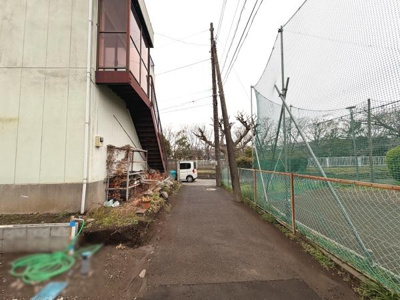 建物の横に広がる舗装された通路があり奥には駐車スペースも確保されています。フェンス越しに隣接するテニスコートが見え周囲は開放的な印象です。必要な設備やスペースがしっかり整っています。