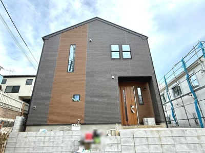 シンプルでモダンな印象の外観です。縦長の窓と木目調のアクセントが目を引きます。落ち着いた色合いで街並みに調和しています。玄関周りがゆったりとしていて開放感があります。