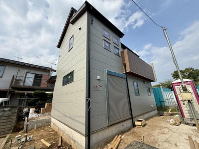シャープな外観デザインが特徴的な建物です。複数の窓配置が室内に自然光を取り入れます。グレーの外壁とシンプルなフォルムが調和しています。玄関部分のシャッターも印象的です。