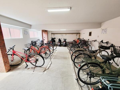 屋内駐輪場には自転車やバイクがしっかりと並び雨風から愛車を守る環境が整っています。明るい照明で夜間も安心して利用可能です。ゆったりとしたスペースがあり出し入れも快適にできます。