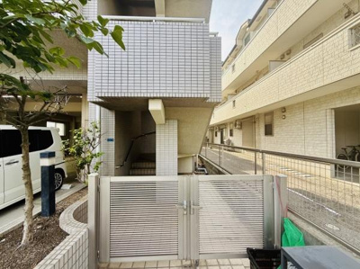 白を基調としたタイル張りの外観が印象的です。門扉と手すりが設置されセキュリティー面にも配慮されたつくりです。複数台の駐車スペースが確保されていて利便性があります。周囲には緑も配置されています。