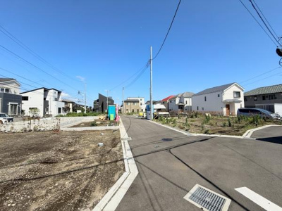 前面道路含む現地写真です。幅のある道路が続き住宅街らしい落ち着いた雰囲気が広がっています。周囲には新しい住宅が立ち並び区画も整っています。視界も開放的で陽当たりの良さが感じられます。