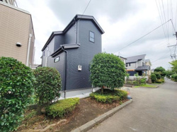 シンプルで落ち着いた色合いの外観が特徴です。周囲の植栽が住まいの魅力を引き立てています。住宅街の中でも存在感のあるデザインが印象的です。道路に面した開放的な立地です。