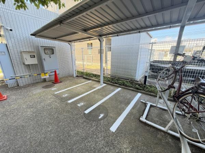 屋根付きの駐輪場で自転車を風雨から守ることができます。明るい日差しが差し込む空間です。区画が明確に分かれており整理された印象を受けます。コーンやフェンスが設置されていて安全性にも配慮されています。