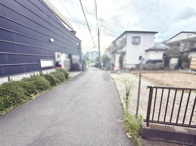 前面道路は舗装されており車両の通行もスムーズです。周囲には住宅が並び落ち着いた雰囲気が感じられます。敷地前に植栽も施されておりきれいに整えられています。