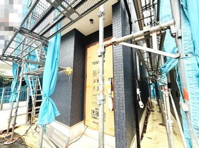 建築中の新築戸建でしっかりとした足場と養生シートが設置されています。前面には車の駐車スペースが確保されており生活動線に配慮された印象です。外観もシンプルなデザインで周囲の住宅と調和しています。