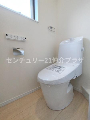 清潔感のあるトイレ空間です。小窓が設置されており自然な明るさが確保されています。壁面にはペーパーホルダーや操作パネルも備わっています。
