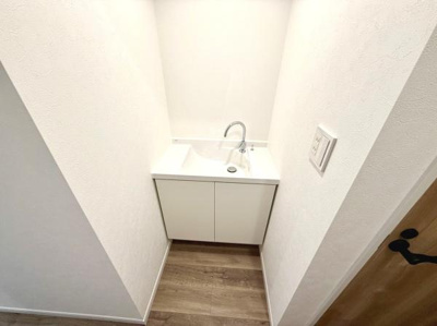 シンプルなデザインの洗面台が空間に無駄なく収まっています。白を基調とした仕上げが清潔感を演出しています。木目調の床がアクセントとなり明るい印象を与えます。