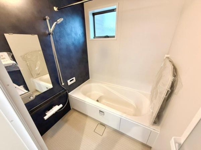 浴室は白とネイビーの落ち着いた配色で清潔感があります。窓が設置されており換気しやすい設計です。大きな鏡とシャワーも付いているため快適に使用できます。床は滑りにくい素材が使われています。