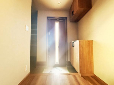 玄関は木目調の収納が備わっており整理しやすい空間です。明るい日差しが差し込み清潔感があります。玄関スペースが広めでゆとりを感じられます。床材と収納の色合いが調和しすっきりとした印象です。