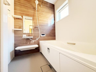 清潔感のあるバスルームです。壁面の木目調デザインが空間に落ち着きを与えています。窓付きで明るい印象となっています。浴槽と洗い場がゆったりとしています。浴室乾燥機が設置されていて快適です。
