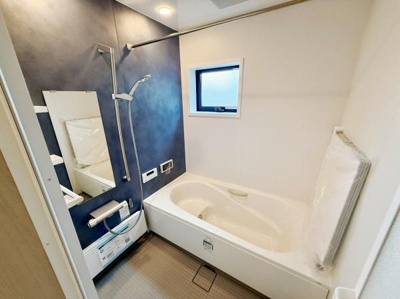 シンプルで使いやすいバスルームです。窓があり換気や採光に便利です。白とネイビーの壁が落ち着いた印象を与えます。浴槽が広くゆったりとした空間が確保されています。収納やミラーも備わっています。