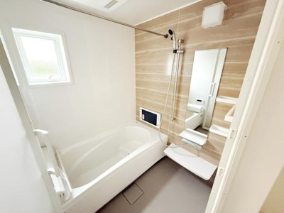 窓付きで明るいバスルームです。壁面の木目調パネルが空間に温かみを与えています。大きな鏡と収納棚が便利に使えます。浴槽はゆったりとしたサイズ感です。床も滑りにくい仕様となっています。