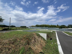 広々とした敷地が広がる現地土地写真です。道路が整備されており周囲には自然の緑も感じられます。青空が広がる開放的なロケーションが特徴です。静かで落ち着いた環境の中でゆとりある空間が確保されています。