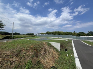 広々とした敷地が広がる現地土地写真です。道路が整備されており周囲には自然の緑も感じられます。青空が広がる開放的なロケーションが特徴です。静かで落ち着いた環境の中でゆとりある空間が確保されています。