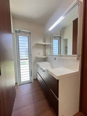 明るい光が入る洗面台が特徴です。広めの鏡が設置されているため身支度がしやすい空間です。木目調の床が空間に落ち着いた印象を与えます。収納も充実しており整理整頓にも配慮されています。