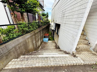 外階段が特徴的な物件です。歩道から玄関までのアプローチがしっかり確保されています。両側に壁や柵があるため安心感があります。周囲に緑があり落ち着いた雰囲気です。建物外壁のメンテナンスも行き届いています。