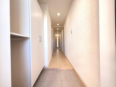 玄関には使い勝手の良いシューズボックスが設置されています。明るい照明で清潔感のある印象を与えます。まっすぐに伸びる廊下が奥行きと開放感を感じさせます。