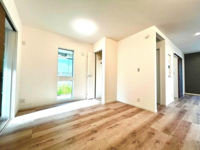 明るい陽射しが差し込むリビングです。白を基調とした内装が空間を広く感じさせます。床材の木目が落ち着いた雰囲気を演出します。収納スペースも確保されています。開放感のあるレイアウトです。